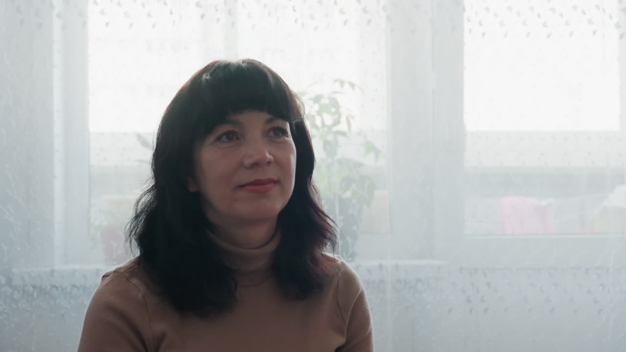 Caucasian Woman Sitting By Window In Soft Backlight, Contemplative To Gentle Smile Sequence, Intimate Headshots For Interview, Counseling, Lifestyle, Cozy Turtleneck, Loose Dark Hair With Bangs, Sheer