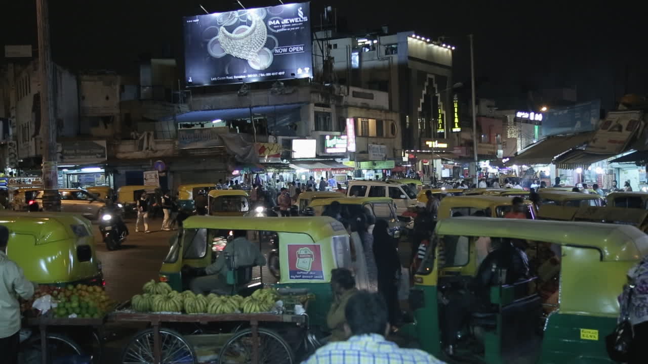 Bustling night traffic with auto rickshaws and crowded street market in Shivajinagar Bangalore