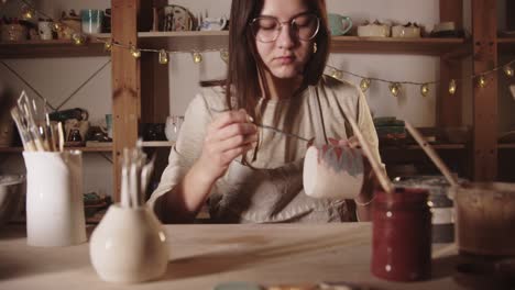 mujer joven alfarero dibujando un diseño en la taza de cerámica con un pincel
