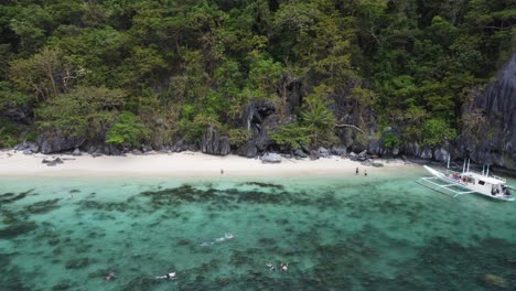 people snorkeling, swimming and sunbathing at paradise beach on cadlao island, el nido