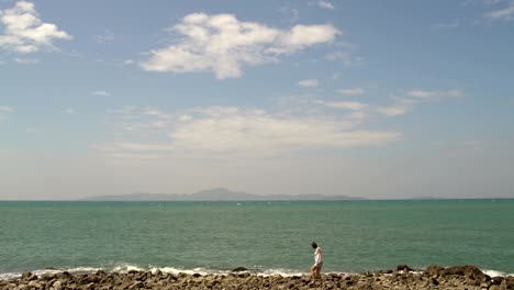 a woman walks along the sea on the rocky shore