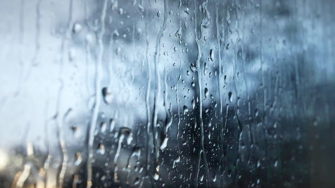 Rainy storm droplets, moody weather fall down window glass closeup bokeh
