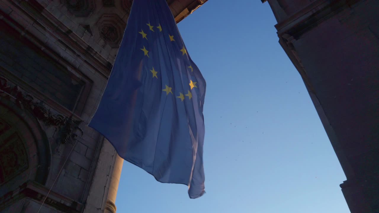 Bandiera europea all'ora d'oro fluttua lentamente tra archi in pietra e il cielo blu