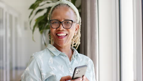 Afroamerikanische-Seniorin-Mit-Smartphone-Am-Fenster-Stehend