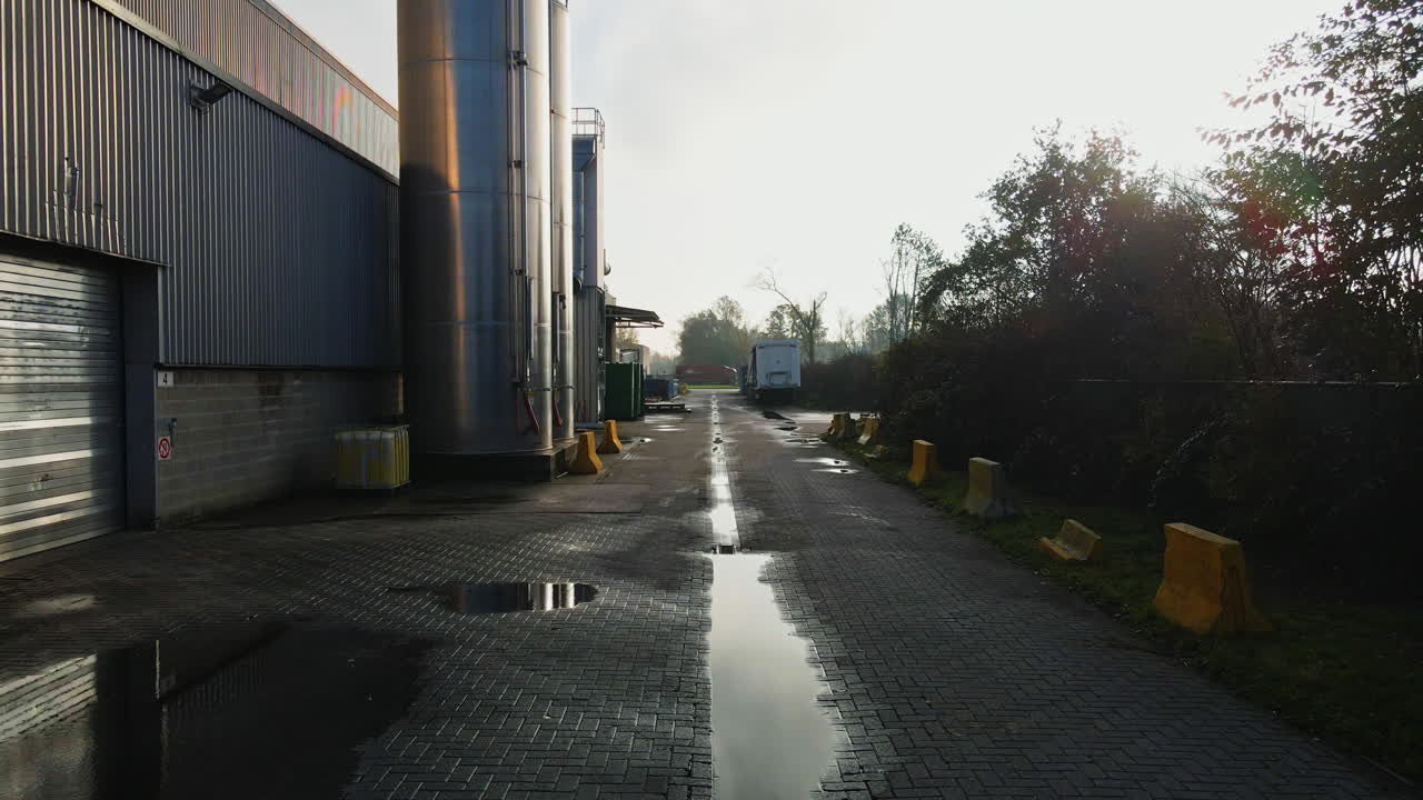 Beautiful dolly in of a factory back lot with tall metal silos and large puddles on the road