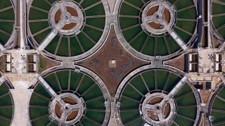 Vista aérea de clarificadores de floculación circulares conectados por pasarelas radiales en una planta de tratamiento de agua potable, formando patrones geométricos con agua verde.