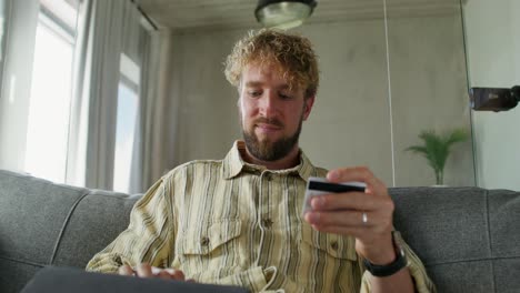 man shopping online using credit card on couch at home