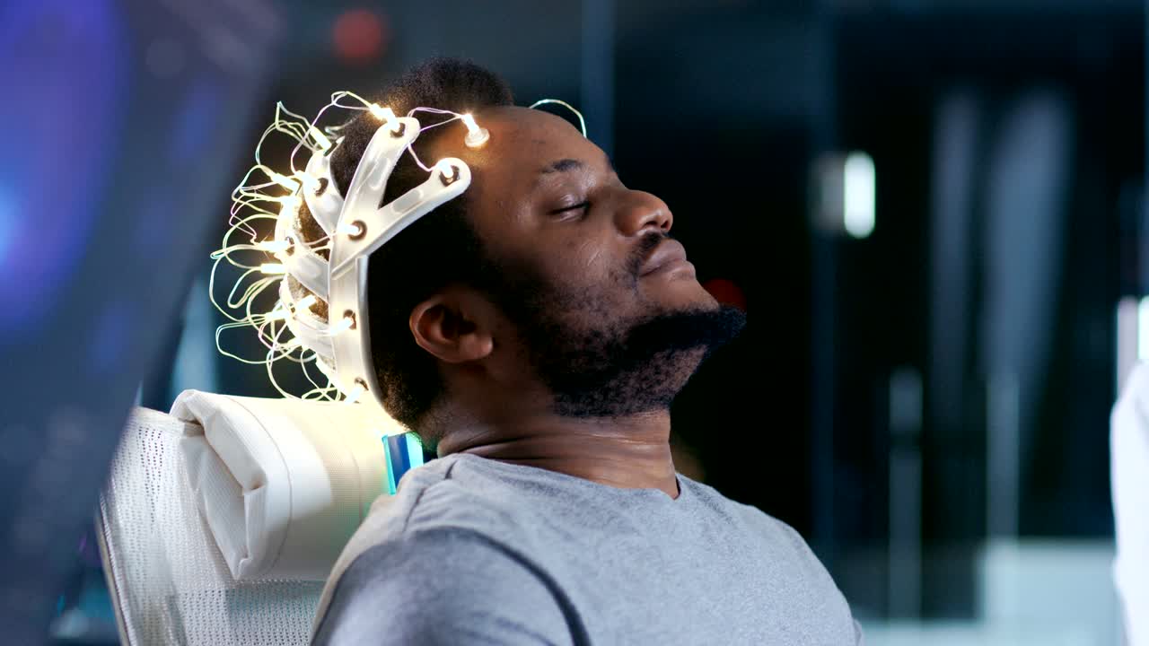 In Laboratory Man Wearing Brainwave Scanning Headset Sits in a Chair with Closed Eyes. Monitors Show EEG Reading and Graphical Brain Model. In the Modern Brain Study/ Neurological Research Laboratory.