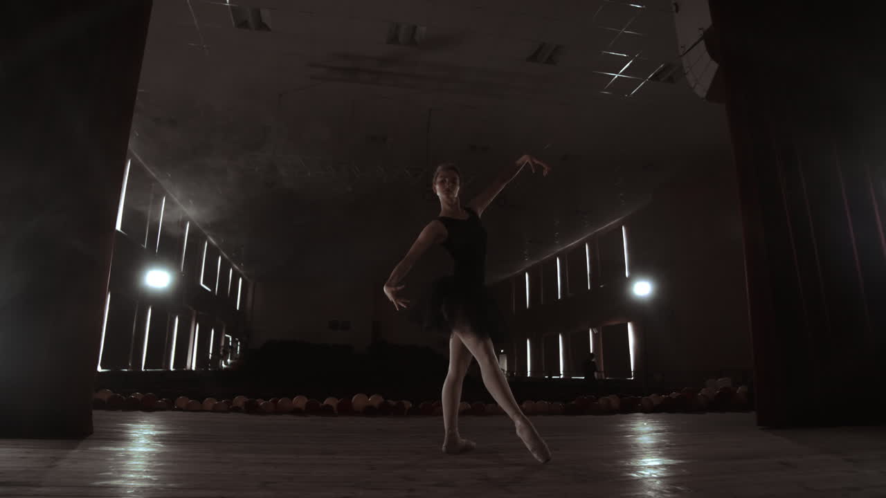 A graceful ballerina dancing ballet elements in the dark with light and smoke on the background slow motion