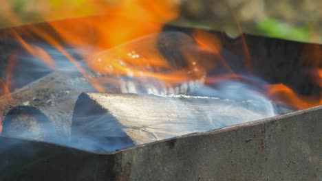 quema de madera y carbones en una parrilla de barbacoa portátil oxidada al aire libre en un día soleado, primer plano