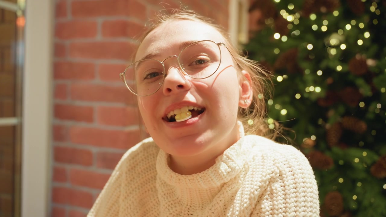 Young Woman Chewing Candy and Smiling by a Christmas Tree