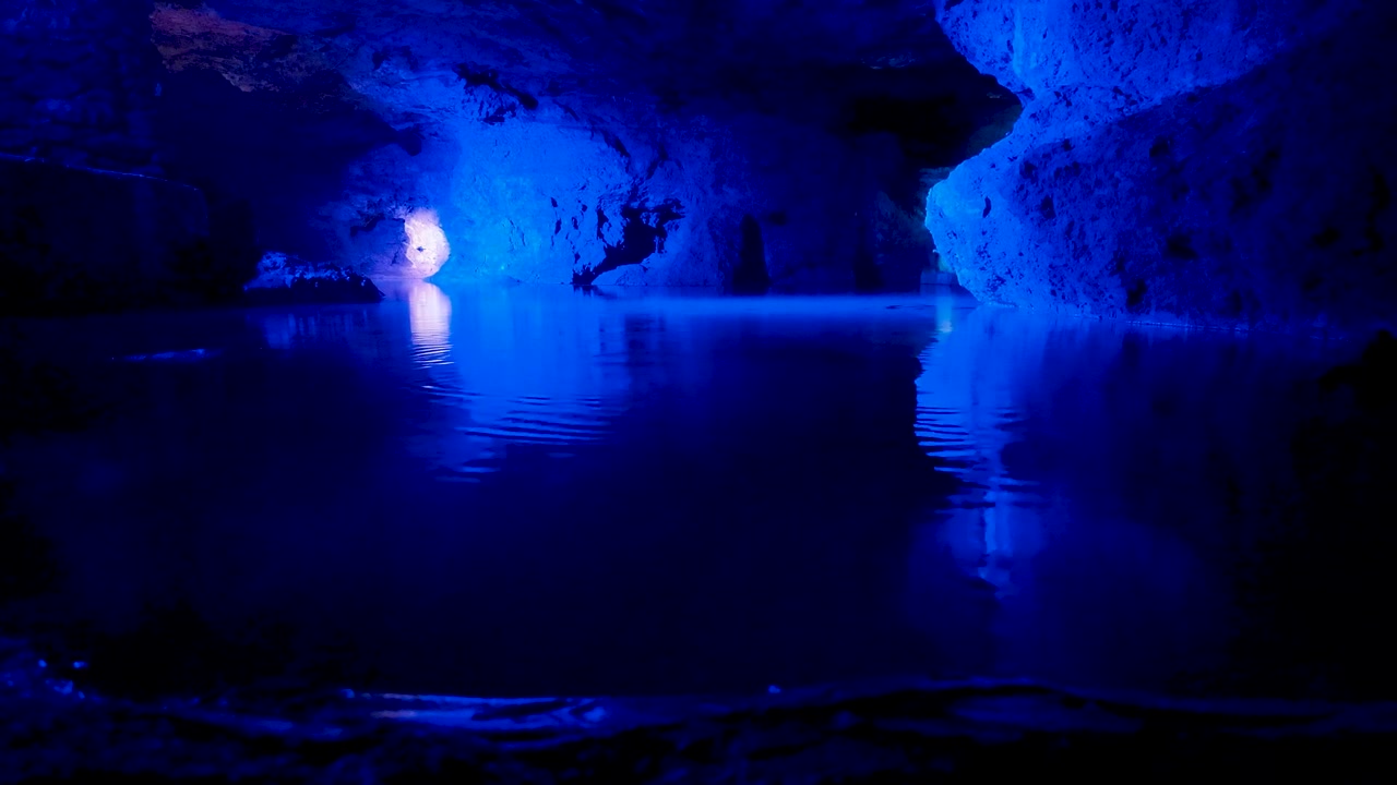 Misteriosa luce blu che illumina una grotta sotterranea con una pozza d'acqua calma. Gocce che cadono dal soffitto creando increspature