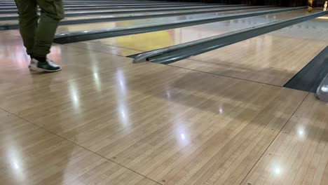 un tipo lanzando una pelota de bolos amarilla a lo largo de una pista.