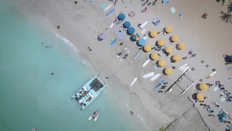 Vista-Aérea-De-Una-Playa-Blanca-Llena-De-Sombrillas-De-Colores-Y-Gente-Relajada-Nadando-En-Un-Mar-Claro