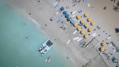 vista aérea de una playa blanca llena de sombrillas de playa de colores y personas relajadas nadando en un mar claro