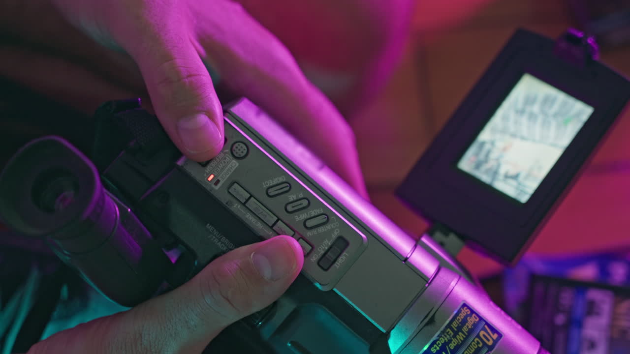 Primo piano di mani che azionano una videocamera vintage con illuminazione al neon