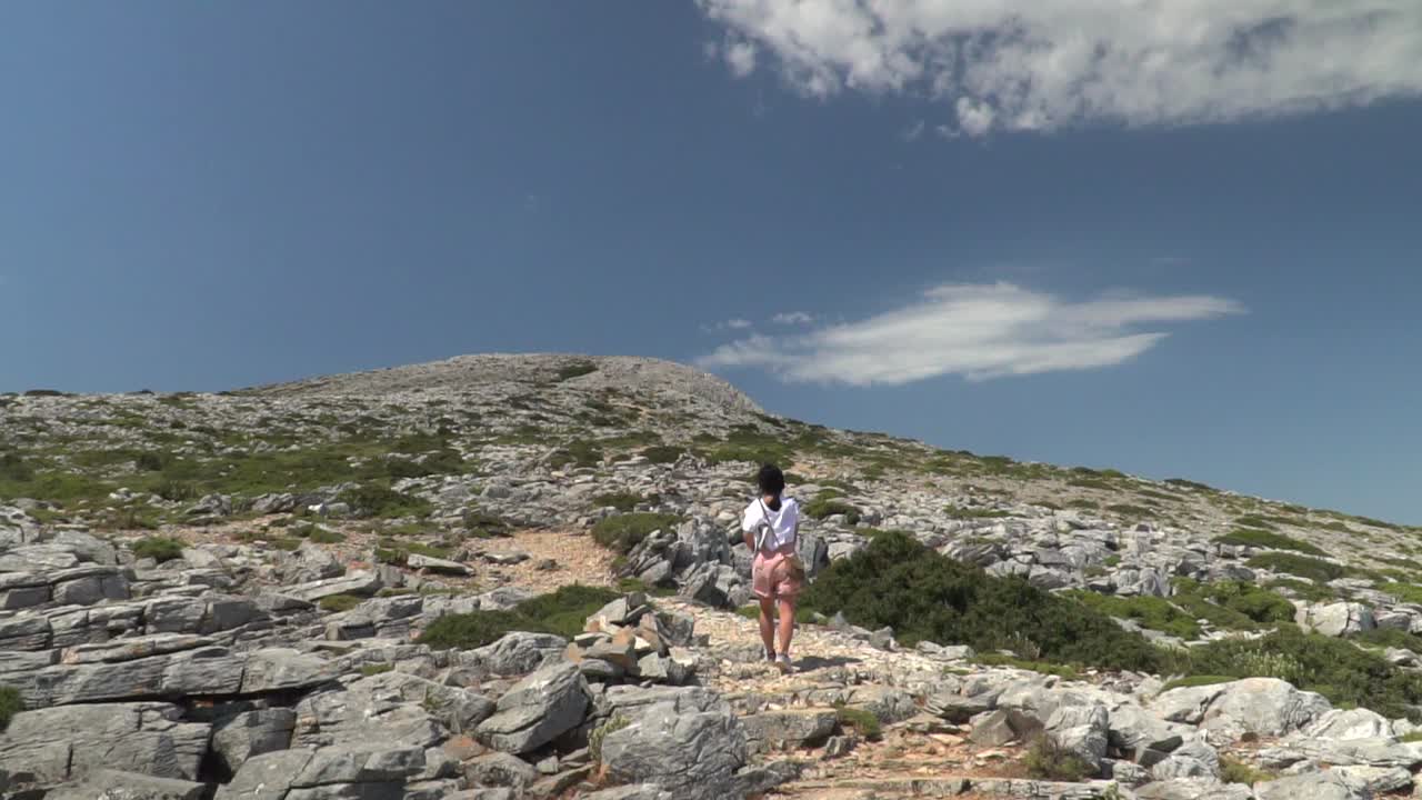 chica en traje de senderismo de verano caminando por la montaña en un paisaje mediterráneo árido