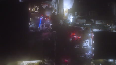 top-down aerial view amidst smoke emanating from a large fire in ste-catherine, québec, canada, at night. the scene captures the scale of the incident and the presence of emergency services.
