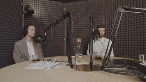 una joven elegante con cola de caballo y un joven apuesto hablan sobre un tema interesante en un estudio de grabación de radio