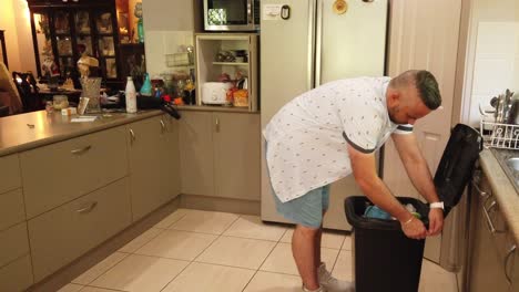 man in the kitchen emptying the kitchen garbage bin to take the trash out to big bin