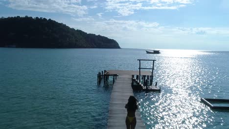 Silhouette-of-a-fit-girl-walking-alone-on-a-pier-in-the-ocean-on-a-tropical-island,-koh-kood,-Thailand