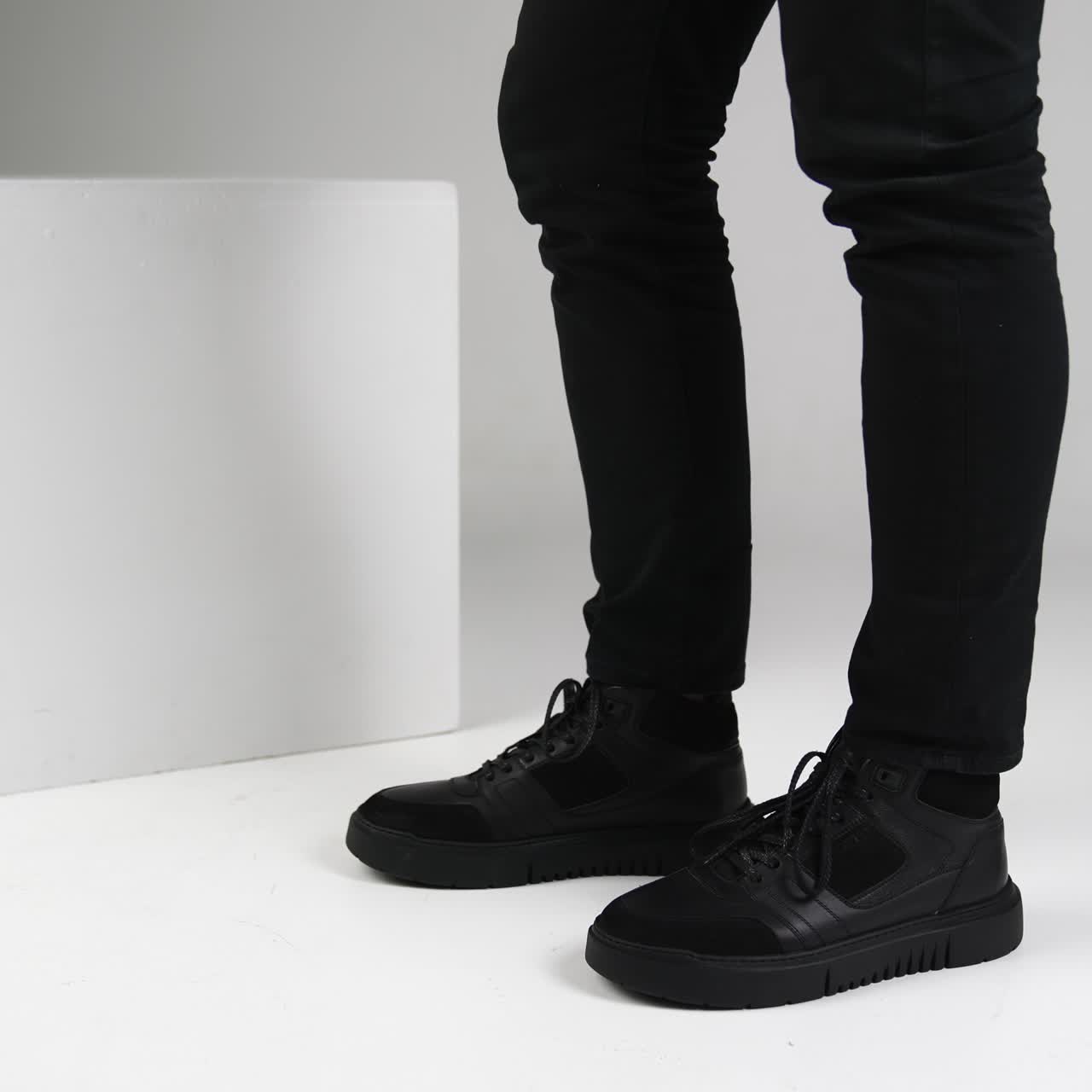 Male model wearing black pants and black footwear. Comfortable fashionable shoes demonstration in white studio