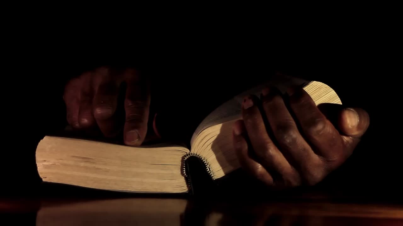 Homme caribéen priant Dieu, les mains jointes, avec une bible et une croix, sur fond noir. Vidéo de stock