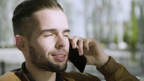 joyful bearded man talking on smartphone outdoor.