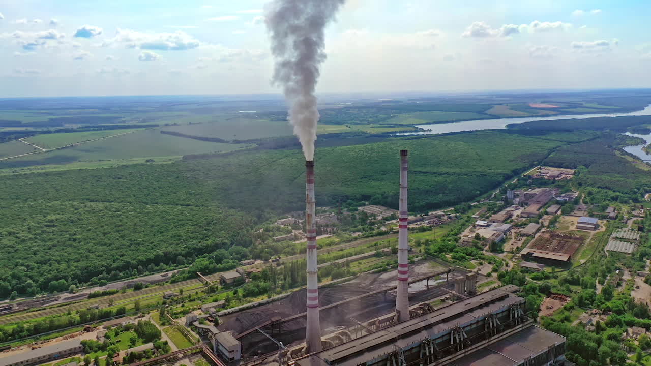 Industrial area in nature. Industrial pipes with smoke. Metallurgical factory with pipes among green field. Aerial view.