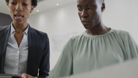 Two-african-american-female-architects-discussing-blueprints-in-office,-in-slow-motion