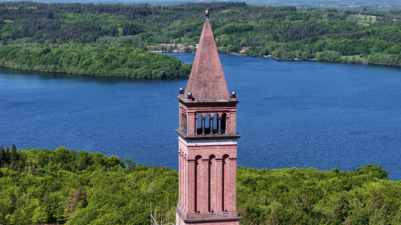 Dramatic aerial footage of the historic Himmelbjerget tower rising above a deep blue lake and green forests in Denmark