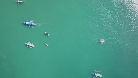 Aerial-view-directly-down-on-emerald-green-waters-with-traditional-filipino-boats-tracking-shot-to-El-Nido-town-in-Palawan,-the-Philippines