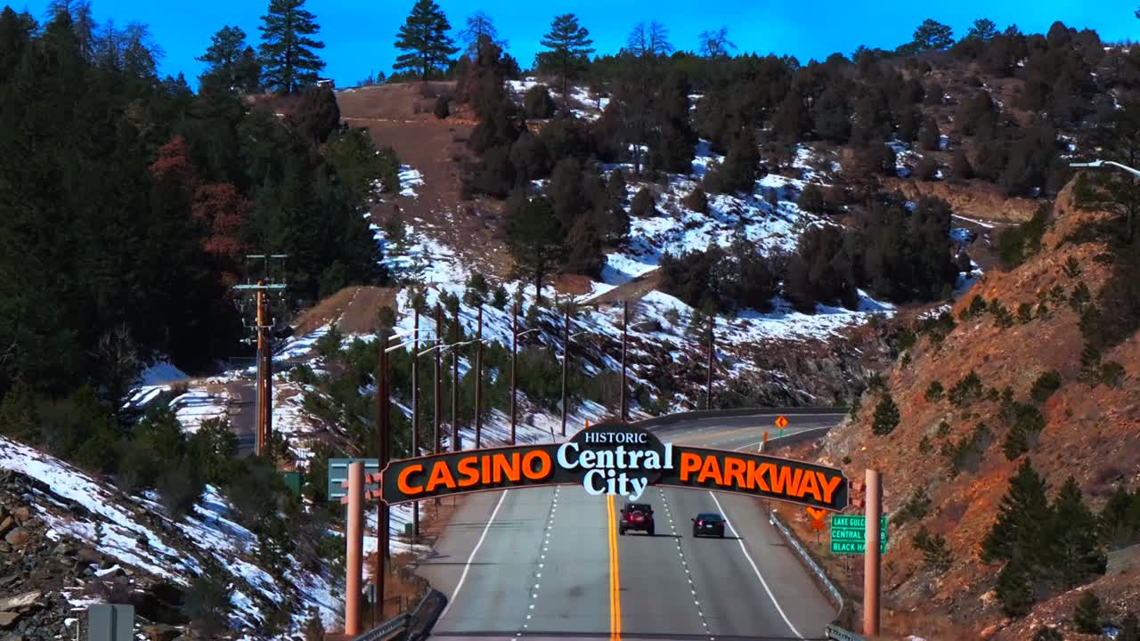 Winter Central City Parkway highway road cars Idaho Springs Blackhawk Colorado aerial drone view welcome sign snow blue sky sunny forest trees Clear Creek Gilpin County slow pan down motion