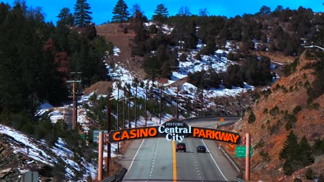 winter central city parkway highway road cars idaho springs blackhawk colorado aerial drone view welcome sign snow blue sky sunny forest trees clear creek gilpin county slow pan down motion