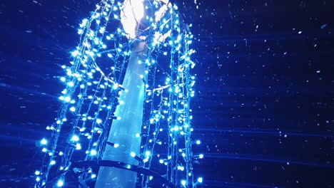 vista de ángulo bajo de la nieve que cae alrededor de las luces navideñas azules que decoran el poste de luz