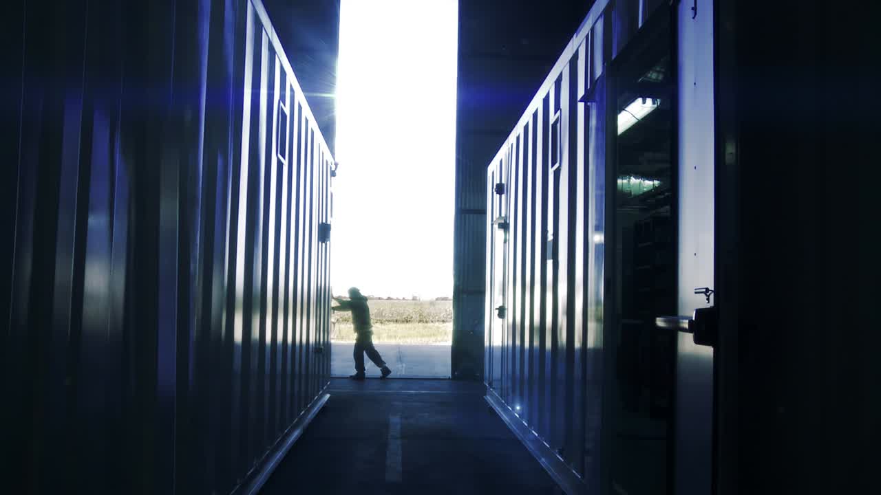 컨테이너 터미널의 금속 문을 열고, 태양 광선이 배경에서 들어오는 익명의 노동자의 내부 시각.