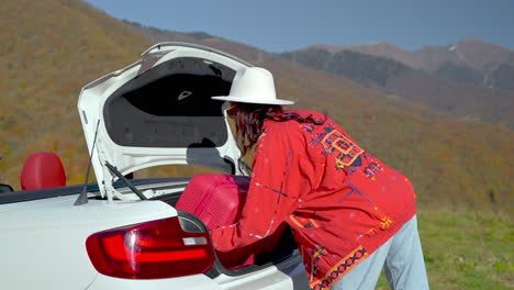 woman packing a convertible car trunk in scenic mountains