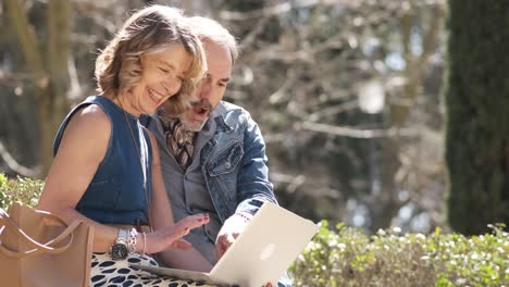 mature couple sitting on stone bench and using laptop