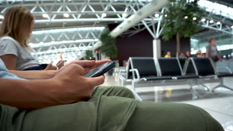 hombre sentado al lado de una mujer en una silla, sosteniendo su teléfono celular y navegando por internet mientras espera en el salón - toma de primer plano