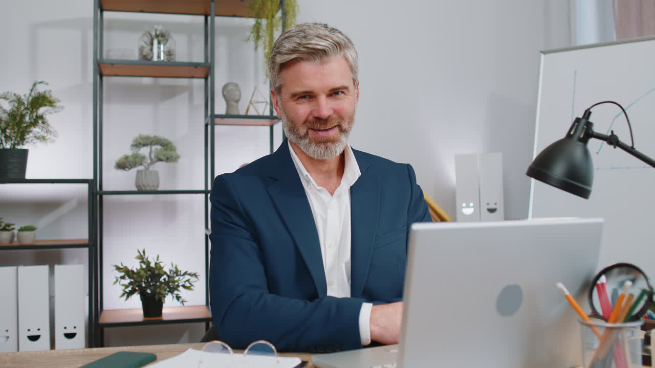 Uomo d'affari che lavora sul portatile dell'ufficio puntando alla telecamera guardando con espressione felice facendo una scelta
