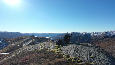 landscape photographer with telezoom and tripod on tall mountain peak during fall season - gentle orbit around person and in front of lens with sunshine and stunning landscape all around - norway