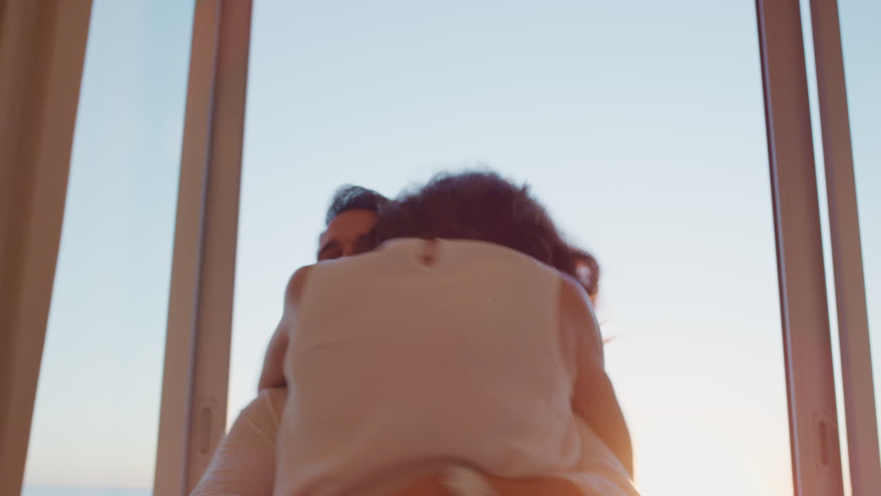 행복한 여행 커플은 신혼여행을 위해 호텔 방에 도착하여 창문 밖을 바라보고 해가 지는 바다의 아름다운 전망을 즐기며  ⁇ 만적인 휴가를 공유합니다.