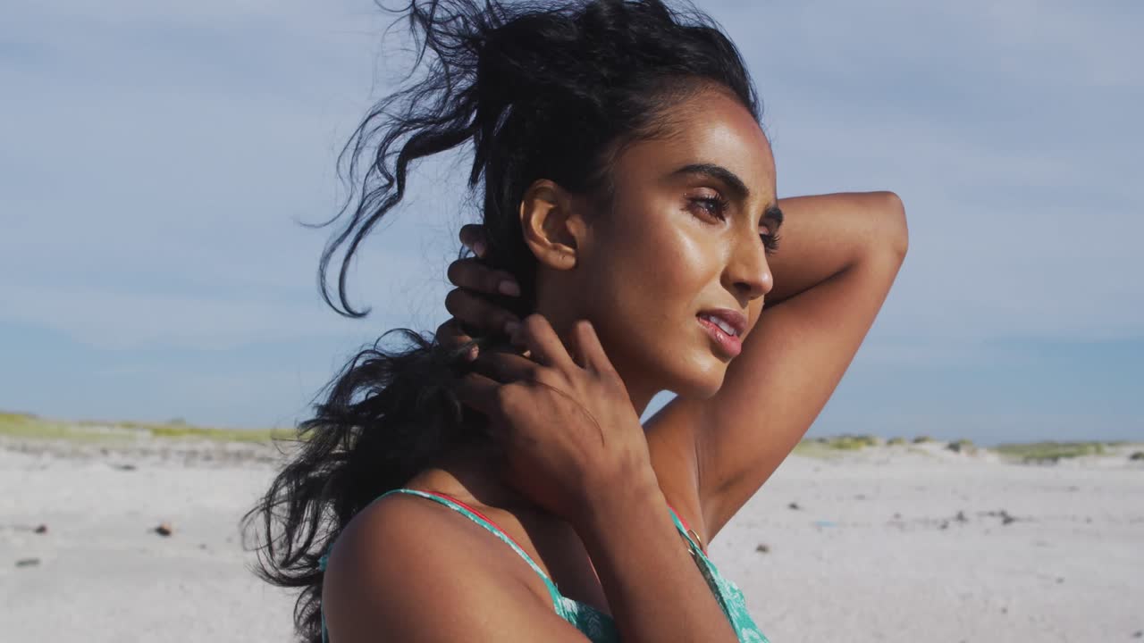 Ritratto di donna ispanica rilassata in piedi al sole e al vento in spiaggia