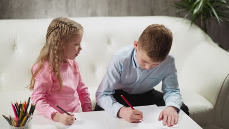 Boy-writes-sister-sits-nearby-on-sofa-studying-together