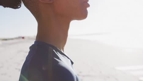 Mujer-Afroamericana-Sosteniendo-Una-Alfombra-Deportiva-Azul-En-La-Playa-Y-Fondo-De-Cielo-Azul