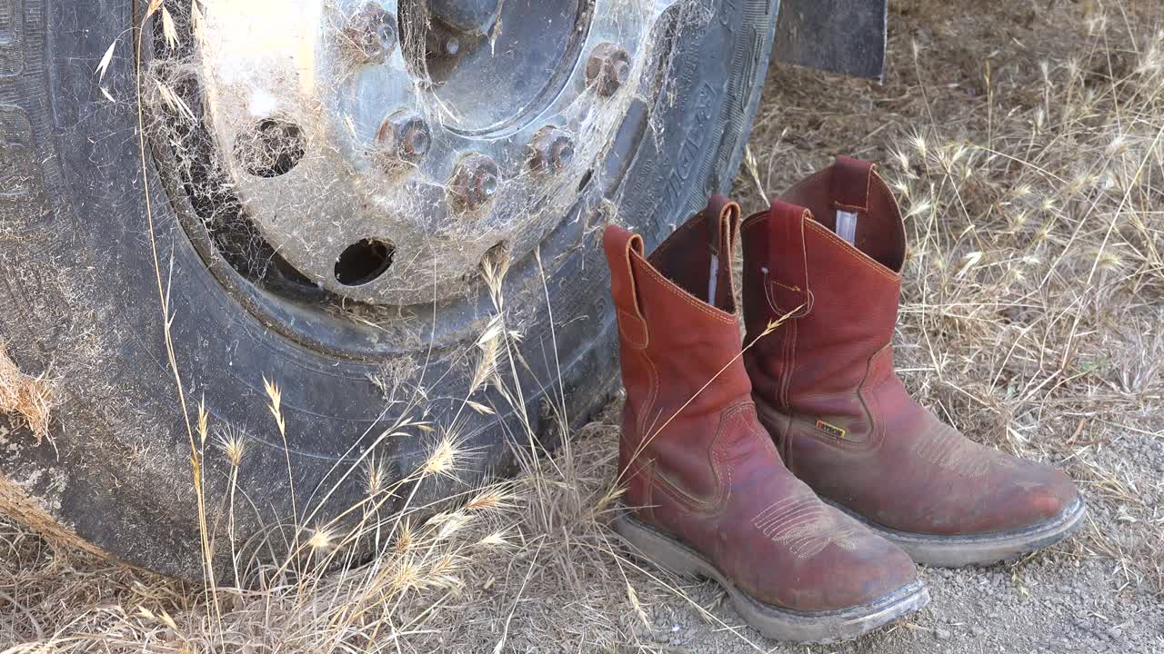 las botas de vaquero se sientan en la base de un neumático de vehículo oxidado como un monumento a un vaquero jubilado
