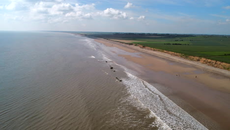 Descending-Establishing-Aerial-Drone-Shot-over-Calm-Sea-with-Flat-Beach-and-Green-Fields-on-Sunny-Day-UK-East-Coast