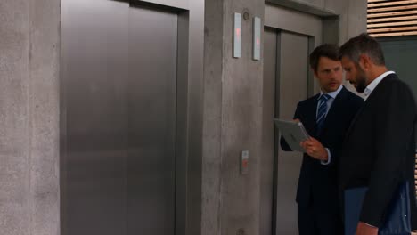 Businessmen-discussing-over-digital-tablet-and-waiting-for-elevator