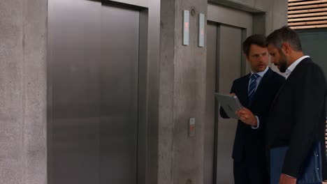 hombres de negocios discutiendo sobre una tableta digital y esperando el ascensor