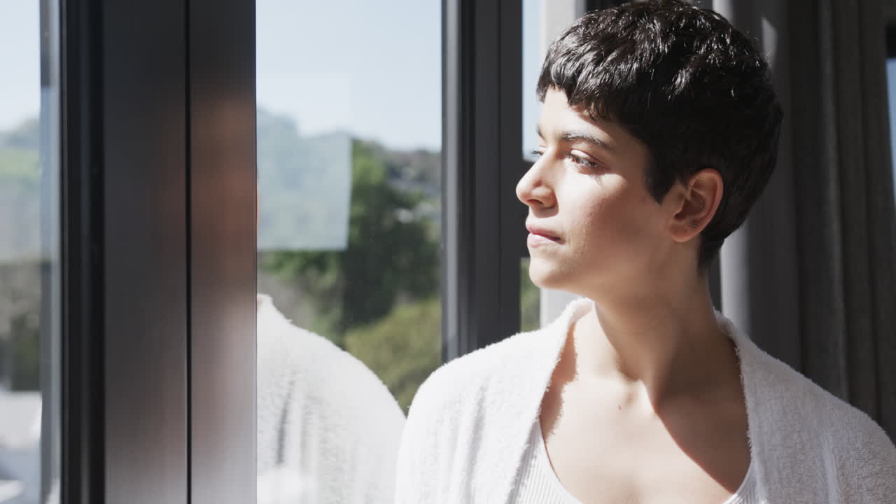 feliz mujer caucásica mirando por la ventana y sonriendo en la casa soleada, copiar el espacio